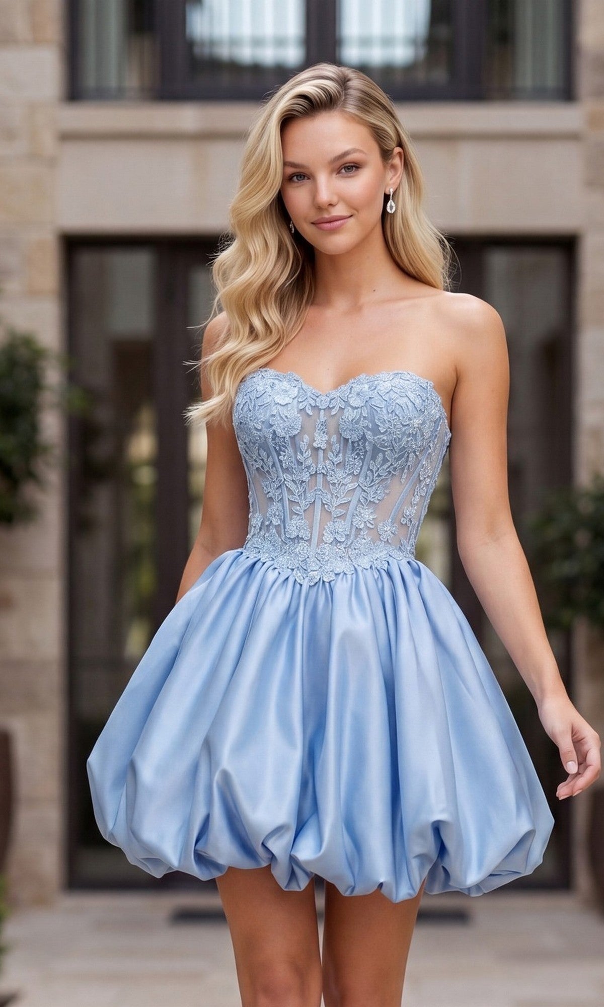 A woman stands outdoors in front of a building wearing the Nox Anabel Q7122 Short Homecoming Dress in powder blue, with a floral lace corset bodice and a voluminous bubble-hem skirt.